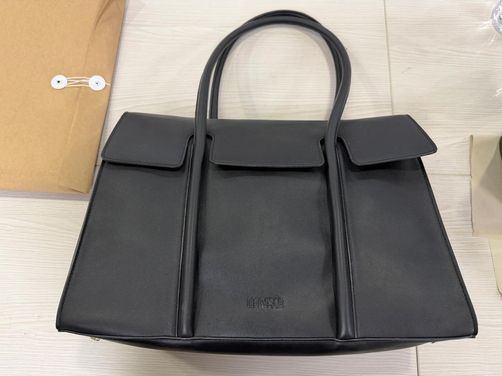 Black genuine leather handbag with twin handles, front panels, and flap details